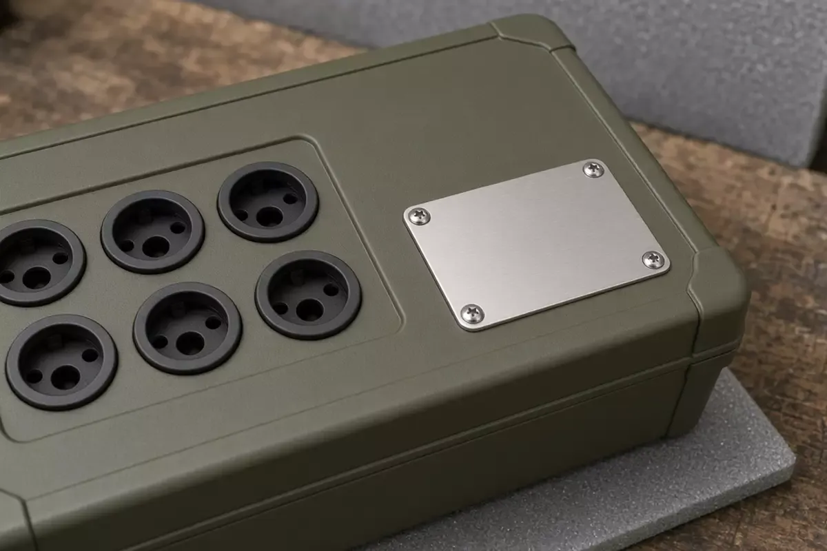 Six black sockets and a blank metal plate on an olive box, resting on gray foam.