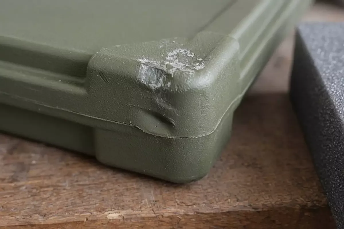 A scuffed olive polymer corner on a wooden bench, with gray foam beside it.